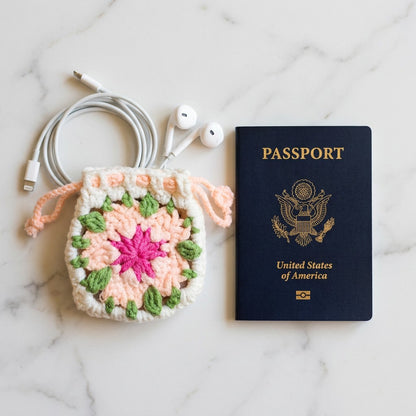 Crocheted pouch with floral pattern, earbuds, and a passport on a marble surface