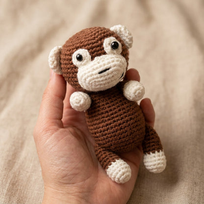 Hand holding a small crochet monkey toy against a beige background