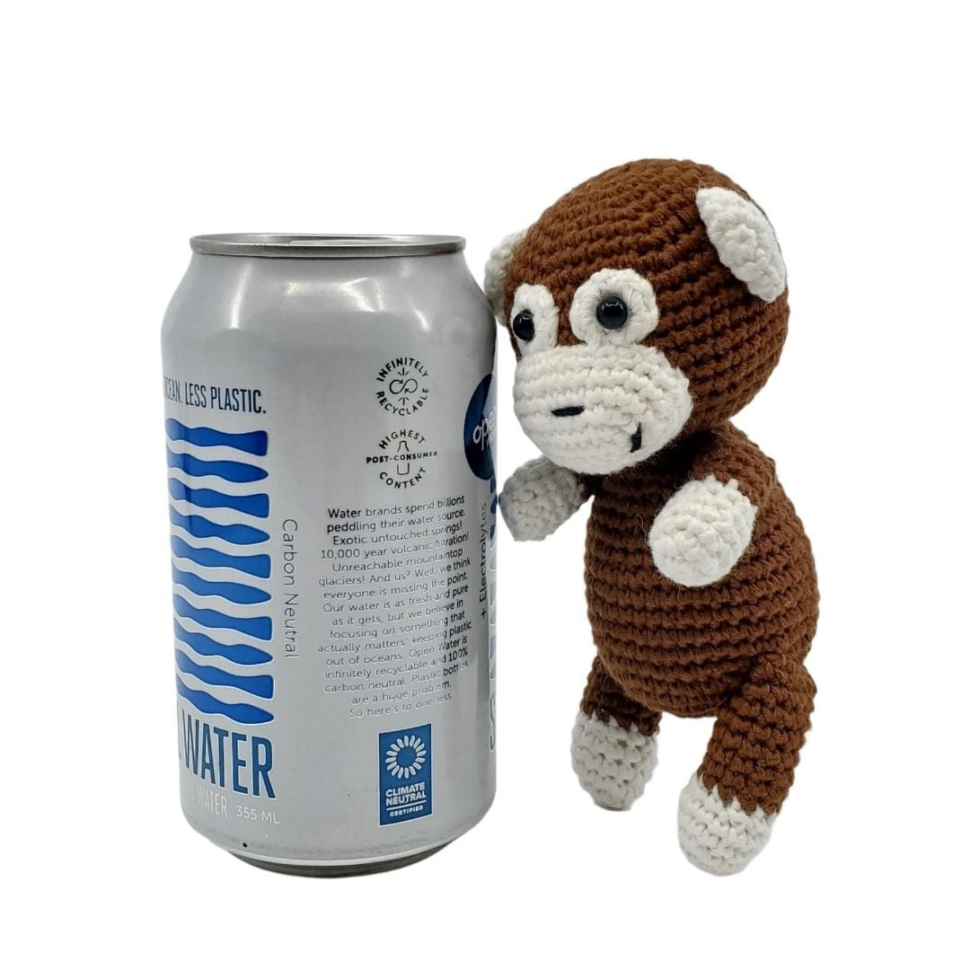 Crocheted monkey toy next to a can of water on a white background
