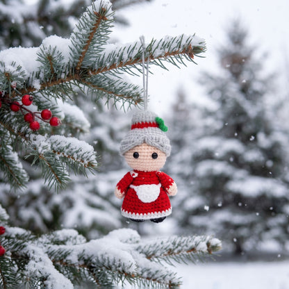 Handmade crochet full body Mrs. Claus ornament by YarnYummies hangs from a snow-covered evergreen branch in a snowy outdoor setting.