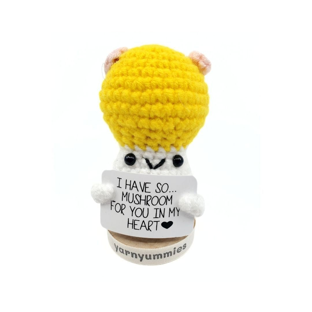Crocheted mushroom character plush toy with a yellow hat and white body, holding a sign.