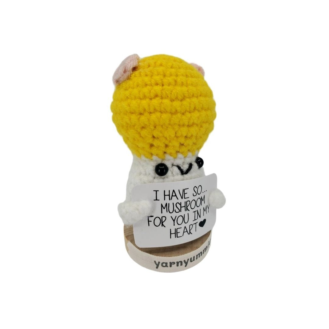 Crocheted mushroom character plush with a heart-shaped tag on a white background