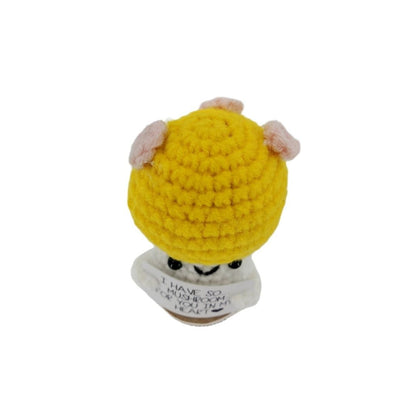 Small crocheted mushroom character plush with a yellow hat and pink ears on a white background