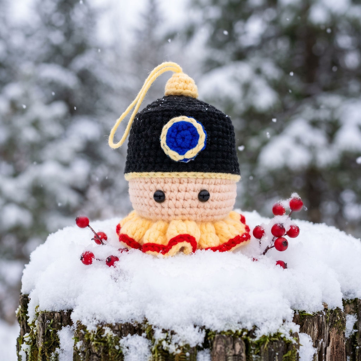 A Handmade crochet nutcracker head ornament by YarnYummies front view showing classic detail in a black and yellow hat with a blue emblem, posed on a snow-covered tree stump outdoors in the snow.
