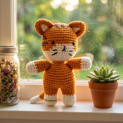 Crocheted tiger toy on a windowsill with a plant and jar in the background