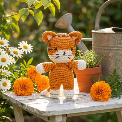 Crocheted tiger toy on a wooden table with flowers and plants in an outdoor setting