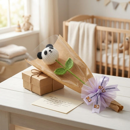 Baby shower gift set with a crocheted panda head on a stem and wrapped with a bow on a table in a nursery.