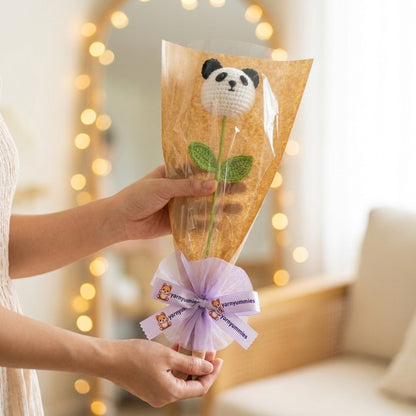 Hand holding a bouquet of knitted panda flowers with a blurred background of lights