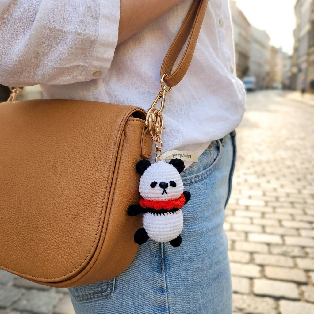 Panda keychain attached to a brown bag on a street.