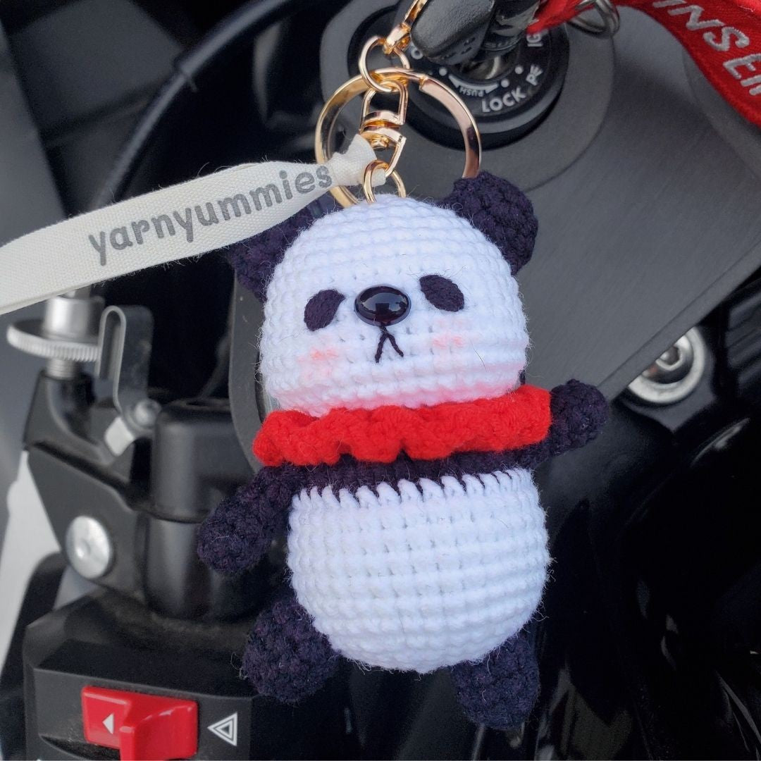 Crocheted panda keychain with a red scarf attached to a motorcycle handlebar.