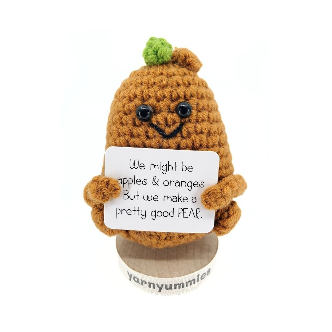 Crocheted pear character holding a sign with humorous text on a white background