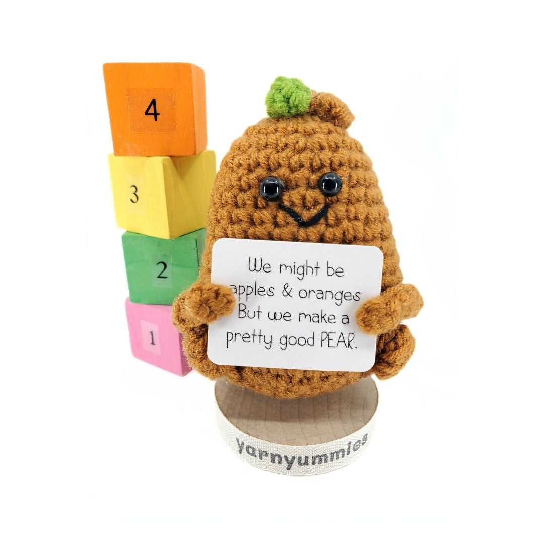 Crocheted pear character holding a sign with text, standing next to colorful blocks on a white background.