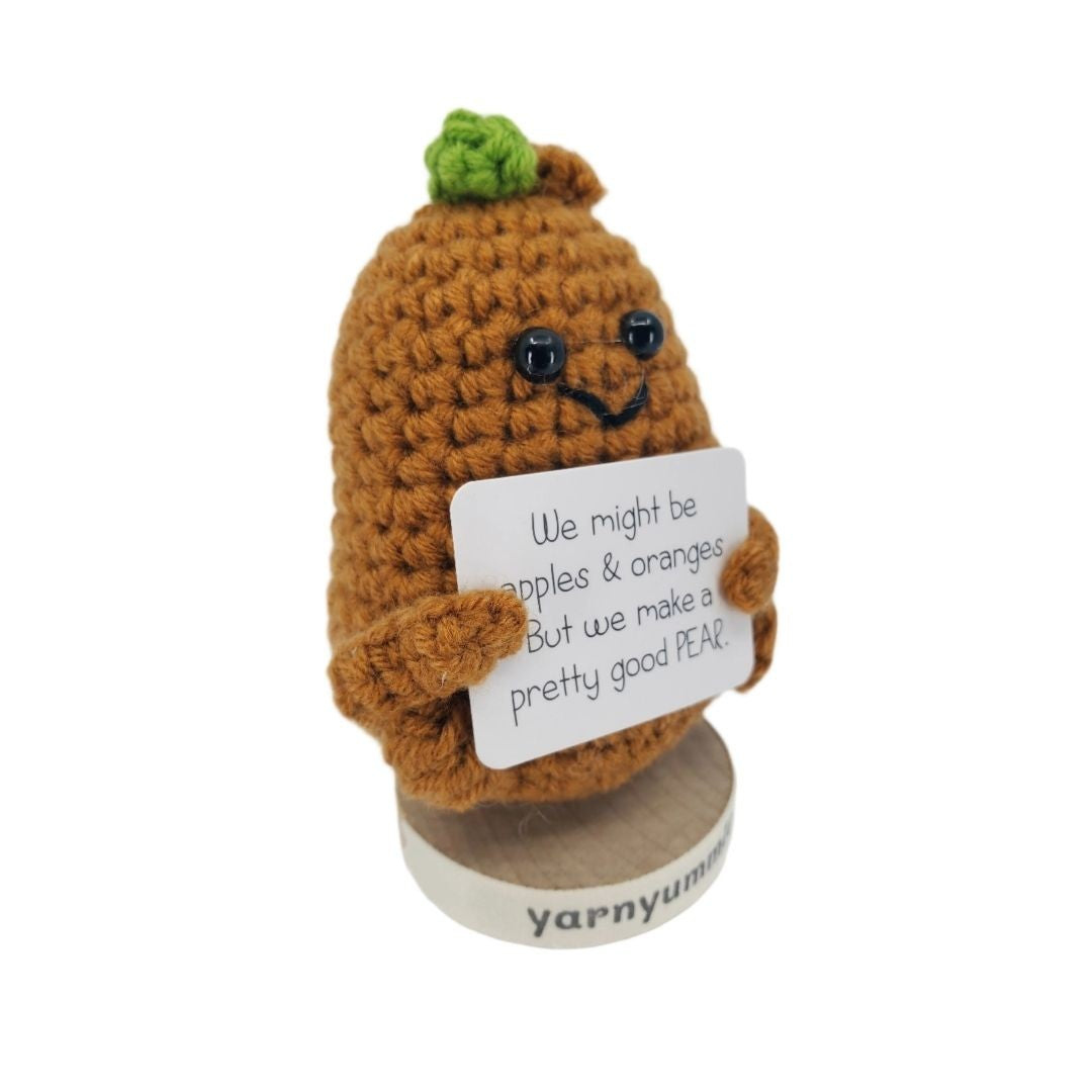 Crocheted pear character holding a sign with text, on a white background