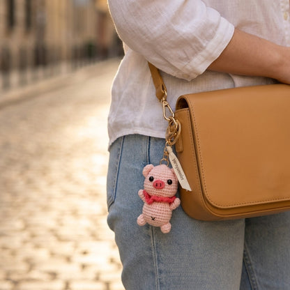 Person holding a brown leather bag with a pink pig-shaped keychain attached, blurred street background