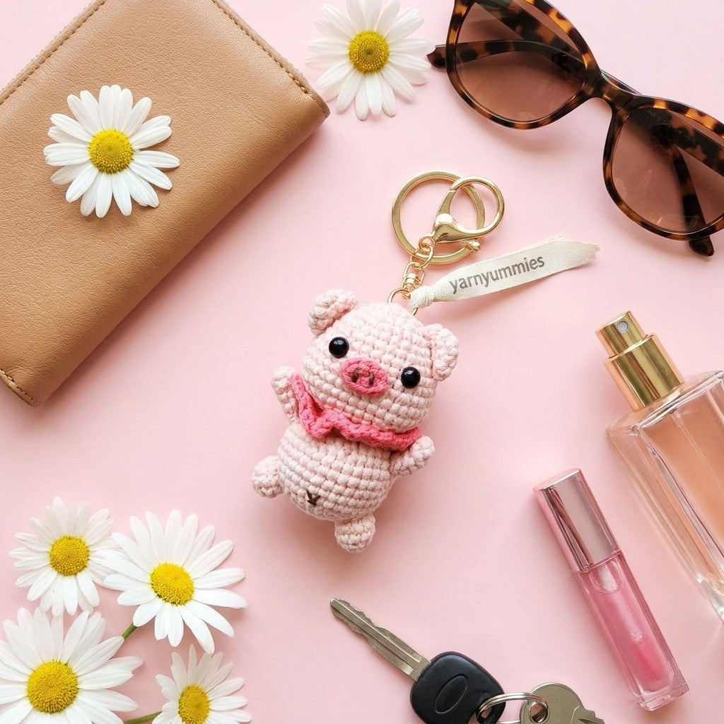 Pig-shaped keychain with pink bow, sunglasses, wallet, daisies, and perfume on a pink background