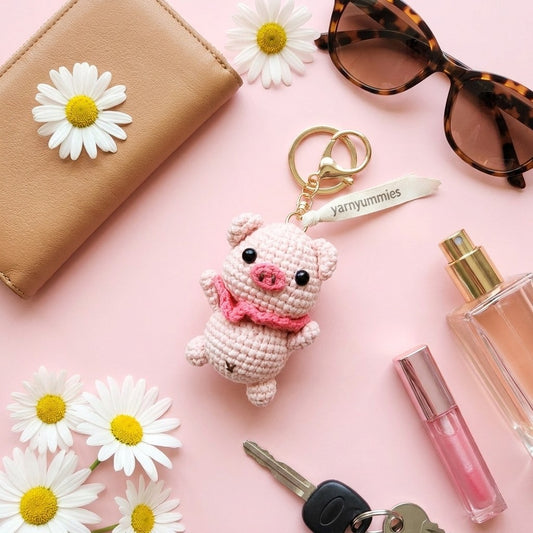 Pig-shaped keychain with pink bow, sunglasses, wallet, daisies, and perfume on a pink background