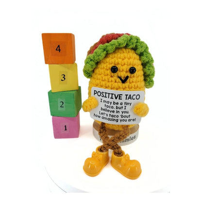 Crocheted taco character with a sign and number blocks on a white background