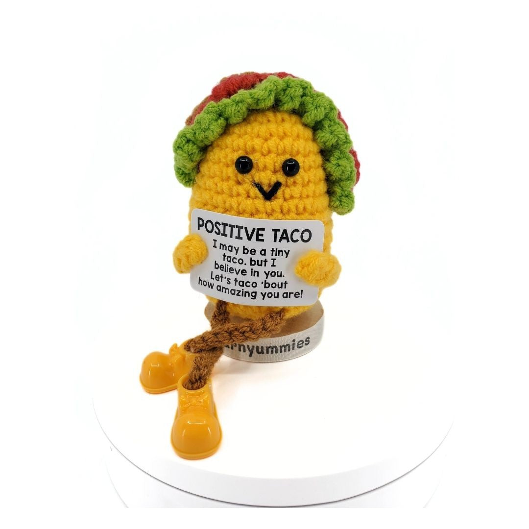 Crocheted toy taco with a sign reading 'Positive Taco' on a white background