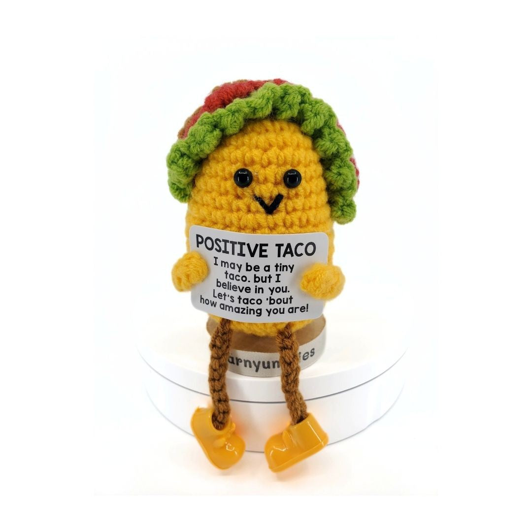 Crocheted taco plush toy holding a sign with text on a white background