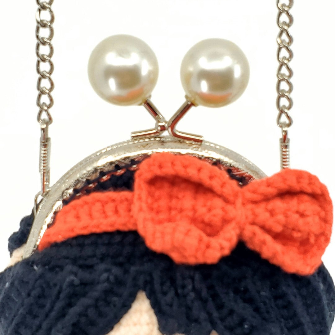 Black knitted bag with a red bow and pearl-like embellishments on a white background