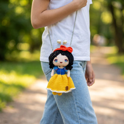 Person wearing a small crochet doll purse with a yellow dress and red hat in a park setting