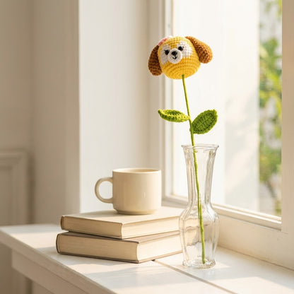 Crocheted dog-shaped flower in a vase on books with a cup and window in the background