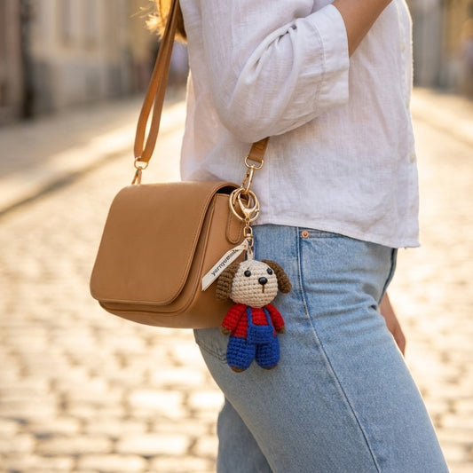 Person holding a tan handbag with a small dog-shaped keychain attached, standing on a blurred street background.