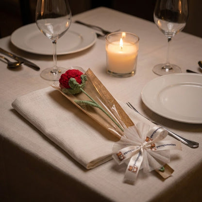 Dining table setting with candles, wine glasses, and a crocheted red rose as a gift.