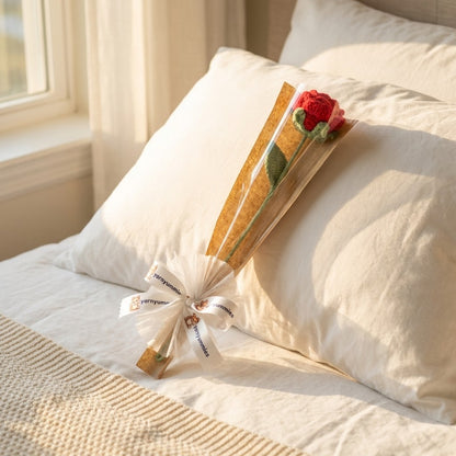 Bouquet of crocheted red rose wrapped in brown paper with a white ribbon on a pillow.