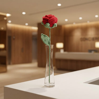 Red knitted flower in a clear vase on a counter with a blurred background