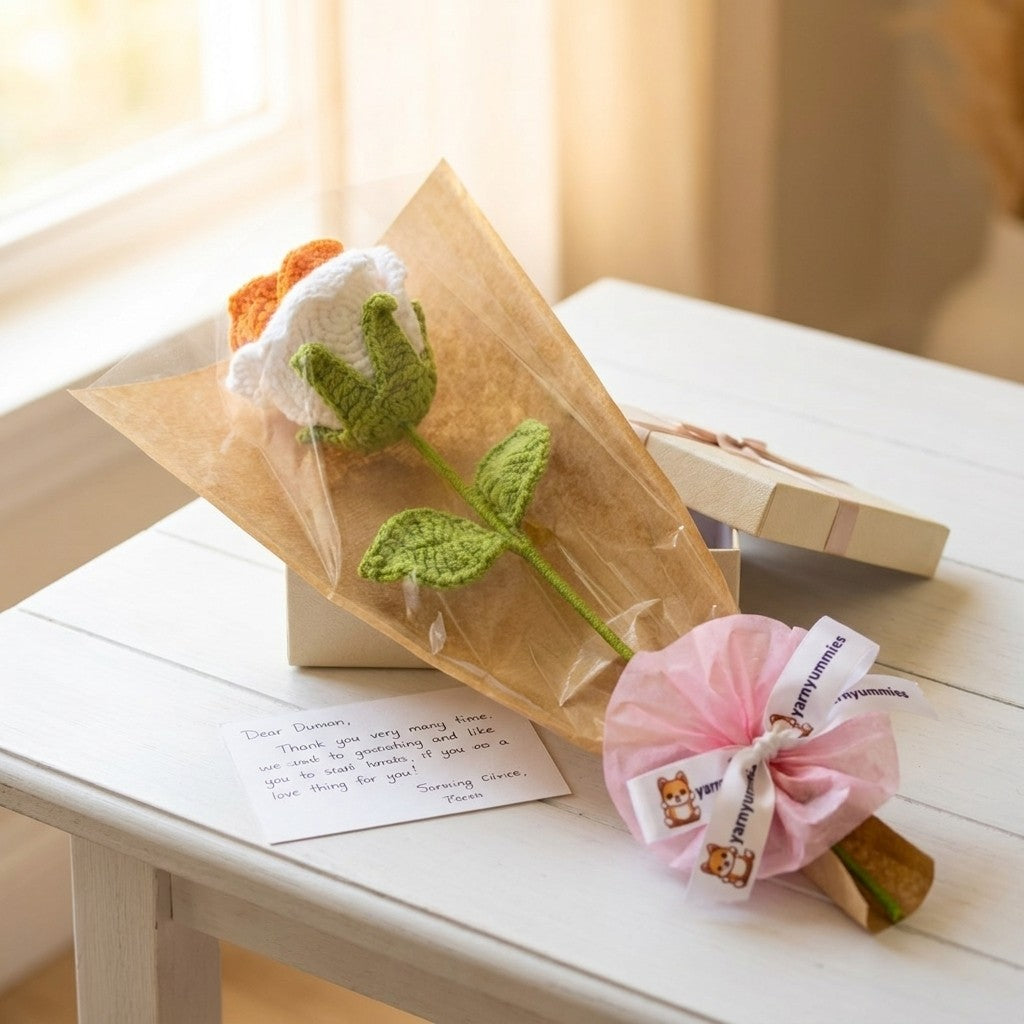 A crocheted rose flower wrapped in brown paper with a pink decorative bow on a white table