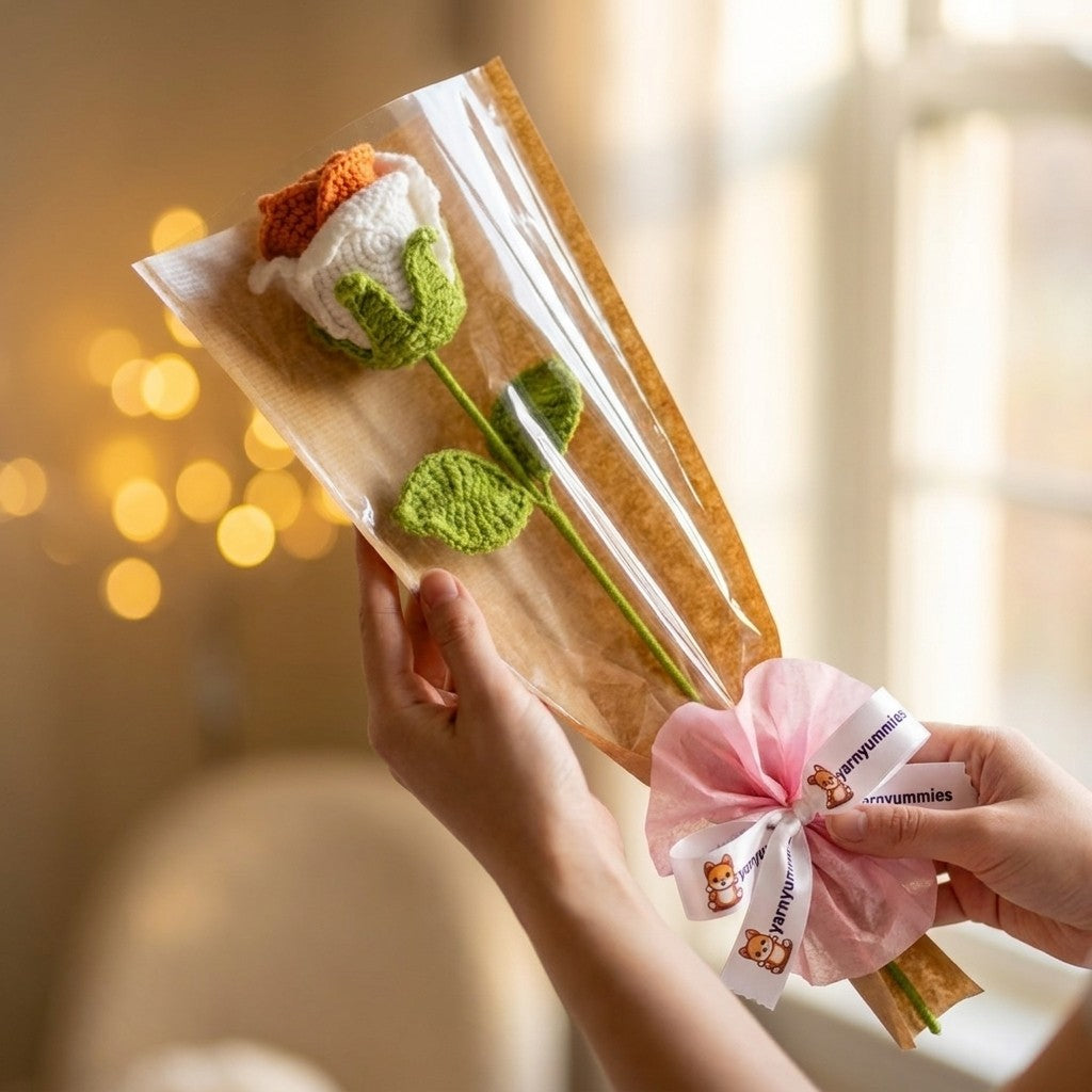 Hand holding a package with crocheted rose flower and a pink bow against a blurred background