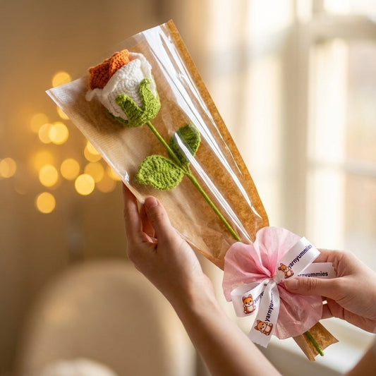 Hand holding a package with crocheted rose flower and a pink bow against a blurred background