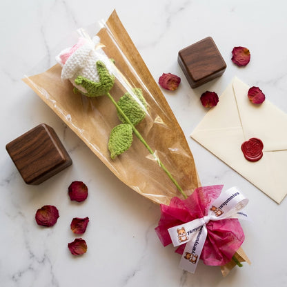 Gift-wrapped item with a pink bow and crocheted rose-shaped object on a marble surface.