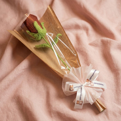 Knitted rose in a clear bag with a decorative bow on a pink fabric background