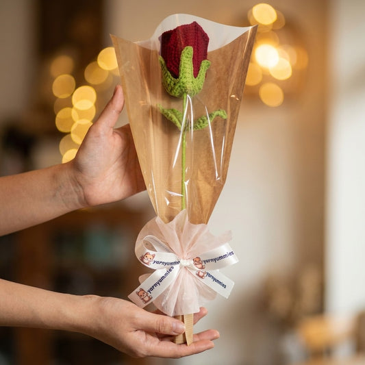 Hand holding a small bouquet of knitted roses with a blurred background