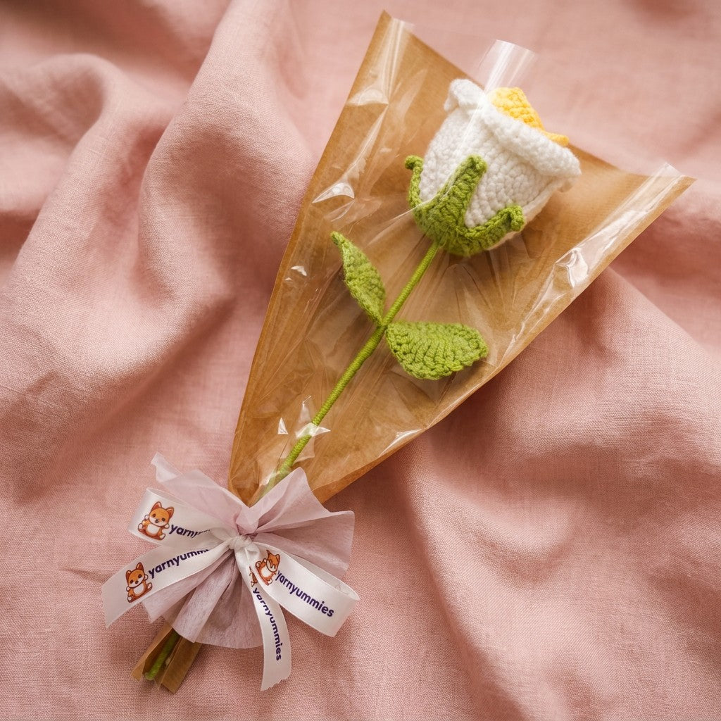 Crocheted white and yellow rose clear packaging with a pink ribbon on a pink fabric background