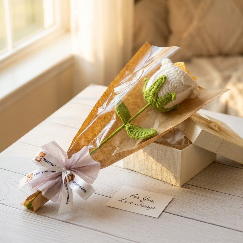 Crocheted white and yellow rose in a clear plastic wrap with a white ribbon on a wooden surface.