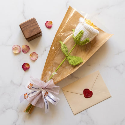Crocheted white and yellow rose with a wooden box and envelope on a marble surface