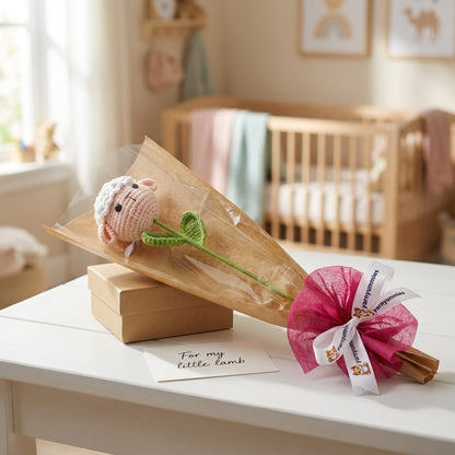 Baby shower gift set with knitted lamb and pink flower on a table in a nursery.