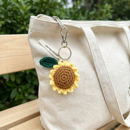 Crocheted sunflower keychain attached to a beige bag outdoors.