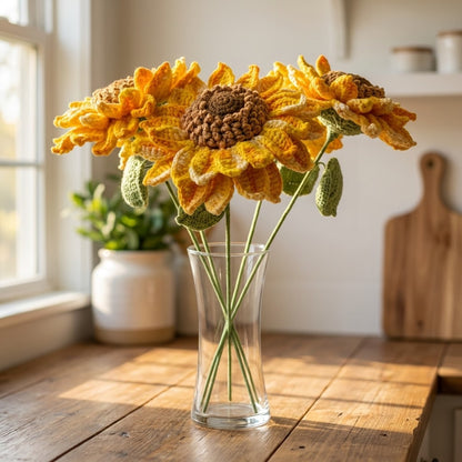 Knitted sunflowers in a glass vase on a wooden table with a window in the background