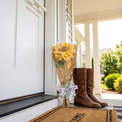 Brown boots and sunflower bouquet on a doormat outside a house.
