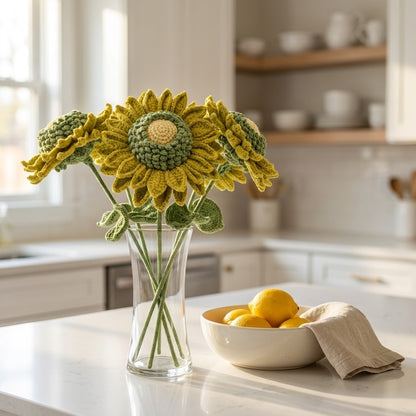 Crocheted green sunflowers in a clear vase on a kitchen counter with a bowl of lemons.