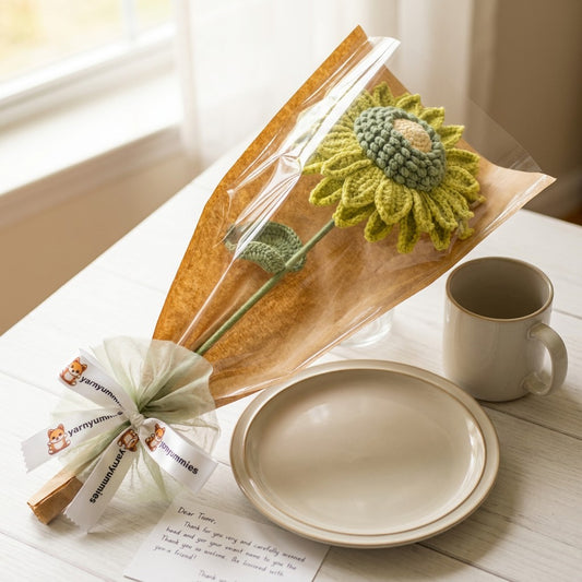 Knitted sunflower in a clear package on a table with a mug and plate.