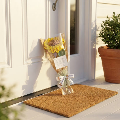 Bouquet of sunflowers on a doormat outside a white door with a potted plant nearby.