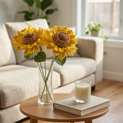 Decorative crocheted sunflowers in a vase on a table with a candle and book in a living room setting.