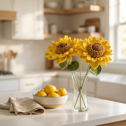 Decorative crocheted sunflowers in a glass vase on a kitchen counter with lemons.