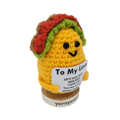 Crocheted taco plush toy holding a card with text on a white background