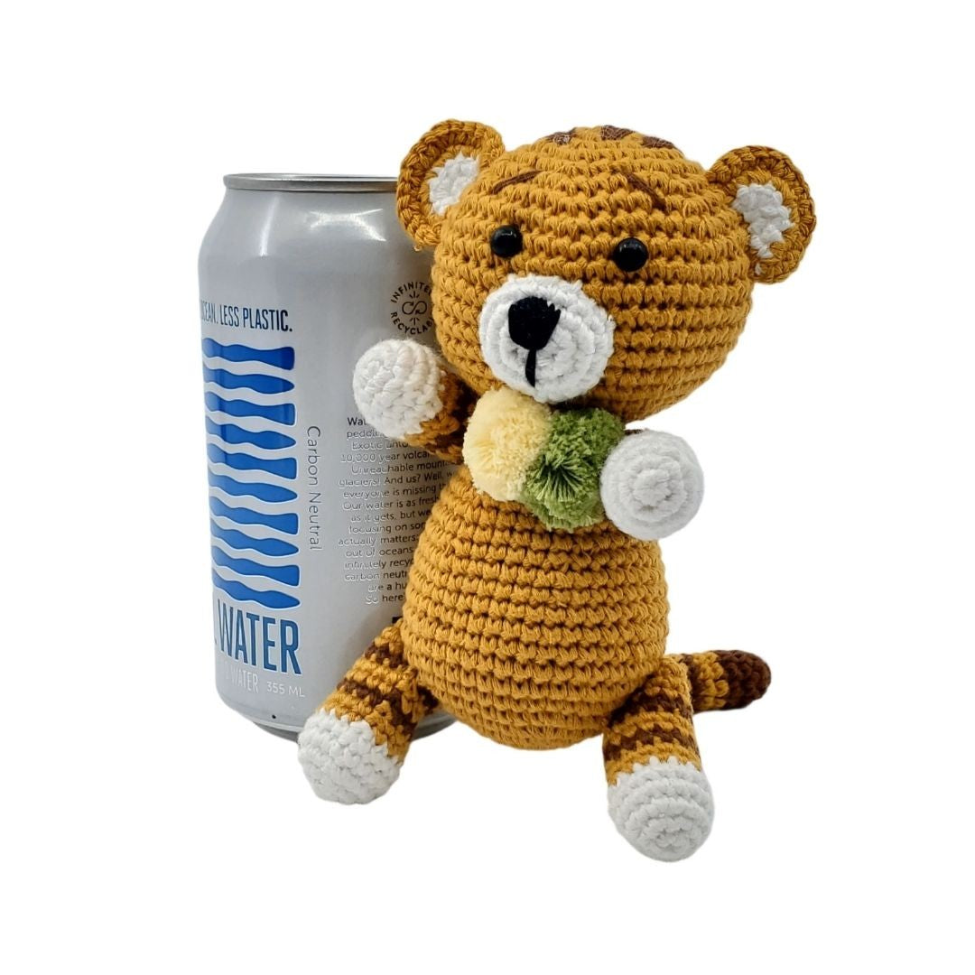 Crocheted tiger toy next to a can of water can on a white background